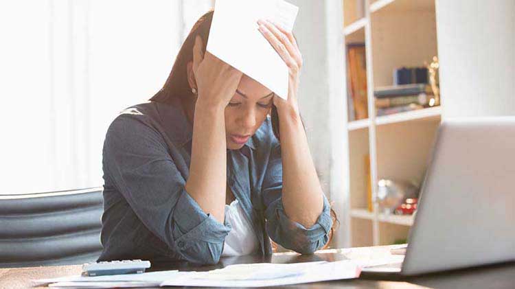 Woman clutching head at laptop.