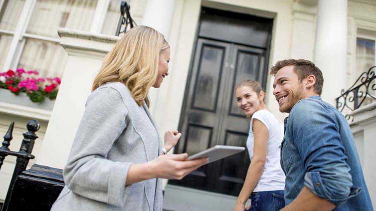 Realtor talking to a young couple on a front porch.