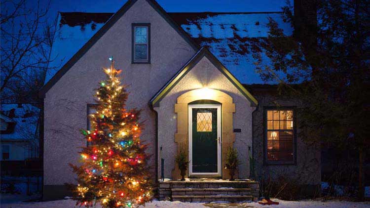 Cozy house in the evening with a lit up Christmas tree outside.