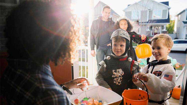 Using Hallowing safety tips, a child dressed as a knight and another as an astronaut are receiving treats.