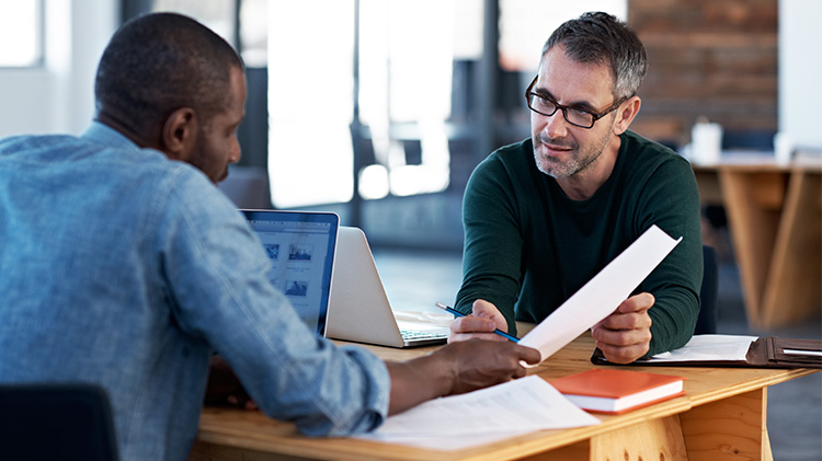 Two men talking about small business benefits and working on a laptop.