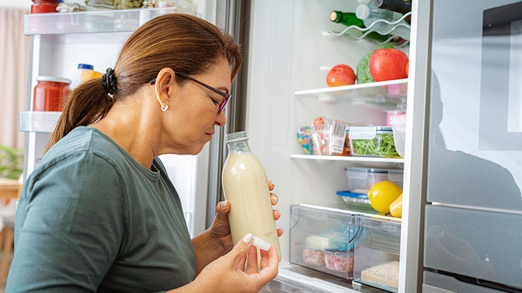Woman smells milk in refrigerator to check for food spoilage.
