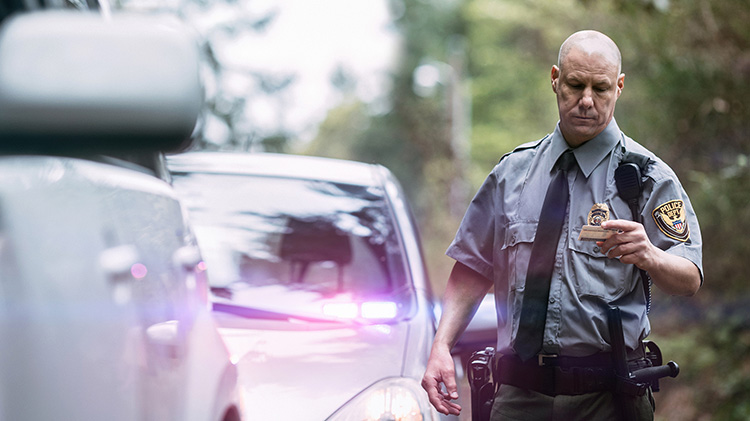 Police officer pulling over car and looking at driver's license.