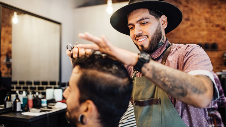 Smiling barber cutting customer's hair in salon.