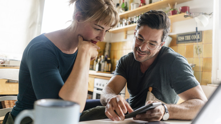 Couple sitting at a table in the kitchen using a smartphone.