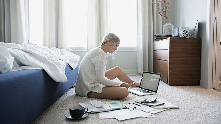 Young woman sitting in the floor reviewing paper bills and in a laptop